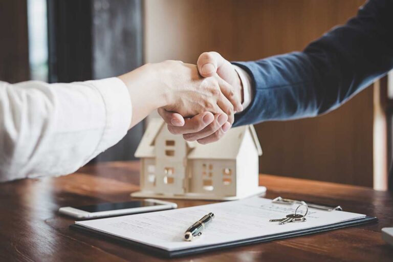A real estate agent and a couple sitting around a kitchen table reviewing a home listing document together.